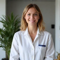 Profesional portrait of a friendly nutritionist, female, with a warm smile, wearing a white coat, in a modern, clean clinic setting with soft lighting, natural background, no text.